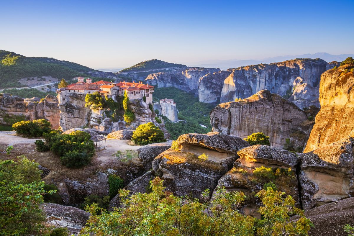 A stunning view of Meteora in Greece, featuring ancient monasteries perched on towering rock formations surrounded by lush greenery and a clear blue sky.